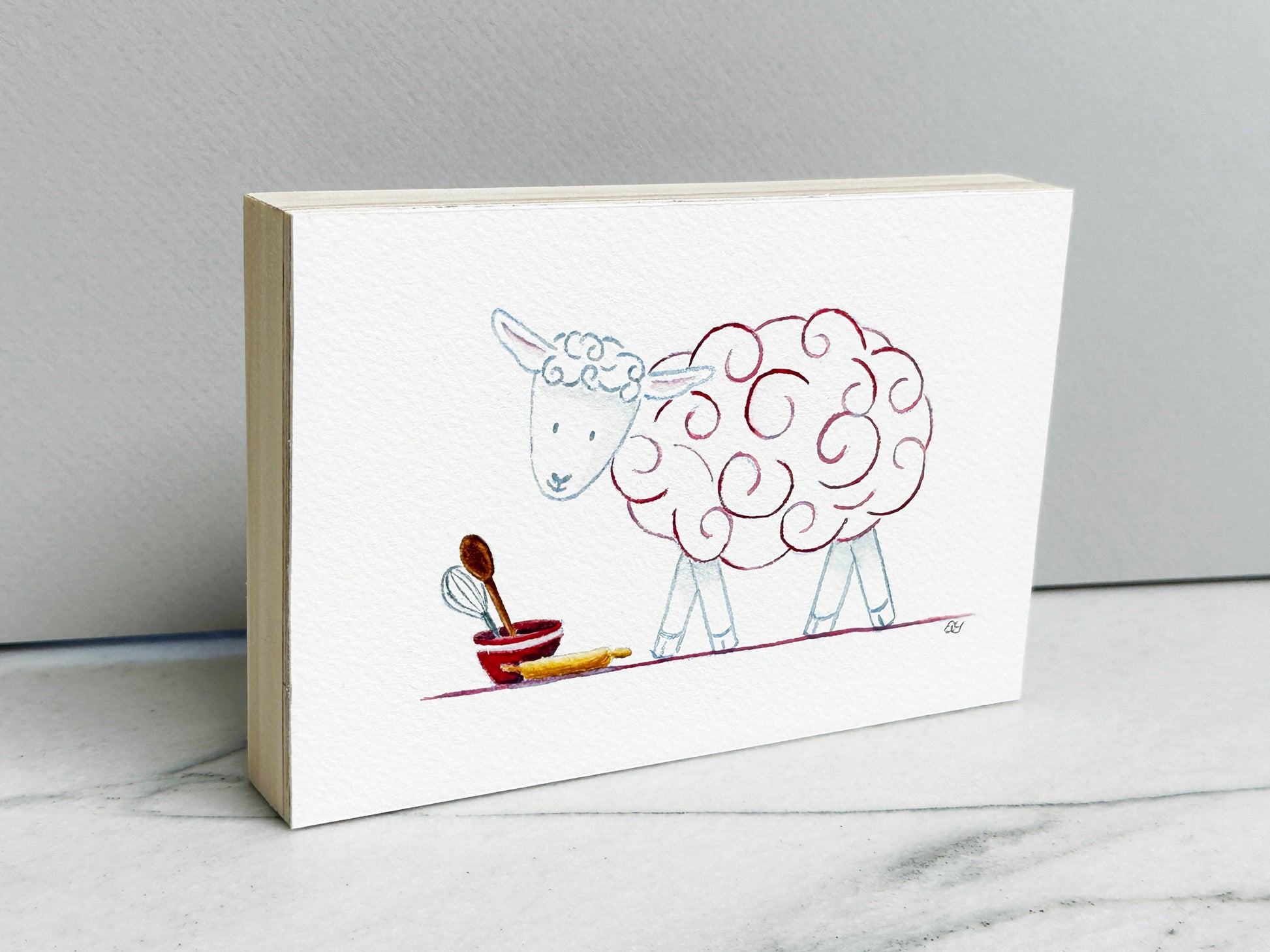 Molly the Sheep, an original watercolor painting of a sheep with raspberry pink curls and baking tools, mounted on a cradled wood panel, side view