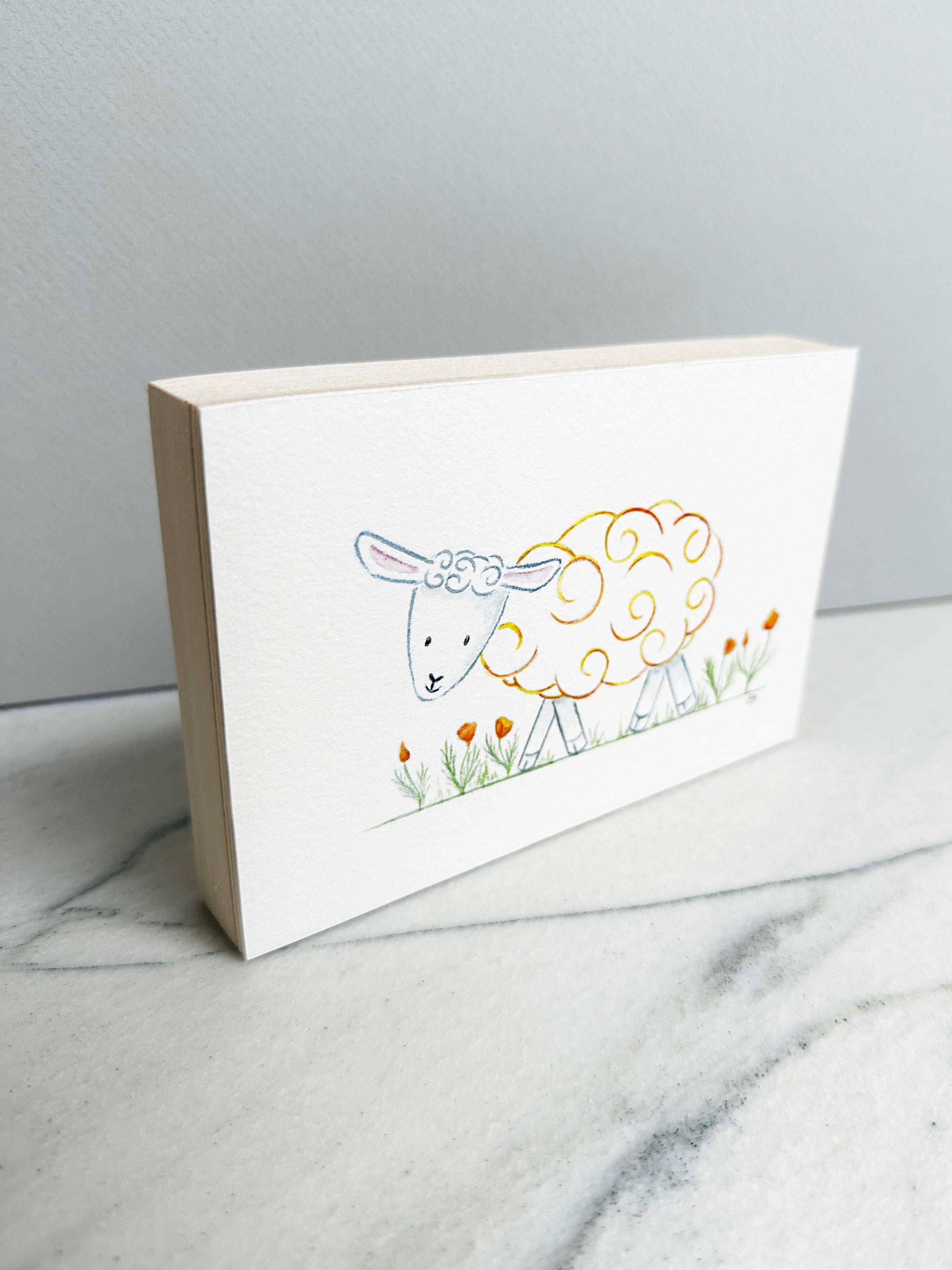 Poppy the Sheep, an original watercolor painting of a sheep with golden yellow curls among orange poppies, mounted on a cradled wood panel, side view